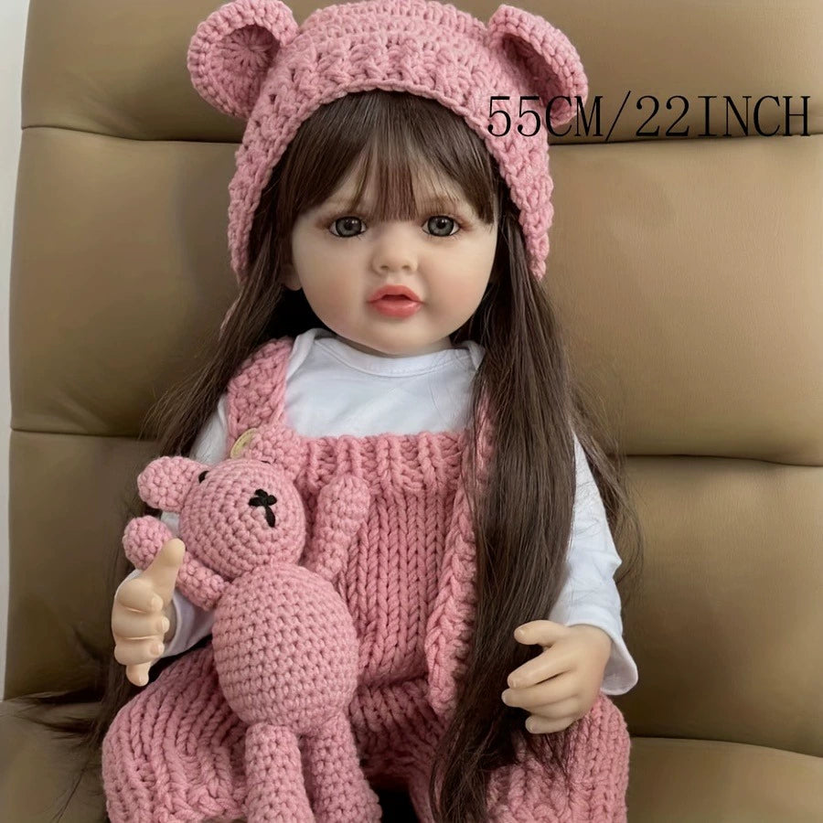 Doll in pink outfit with bear hat and toy, sitting on a brown chair.