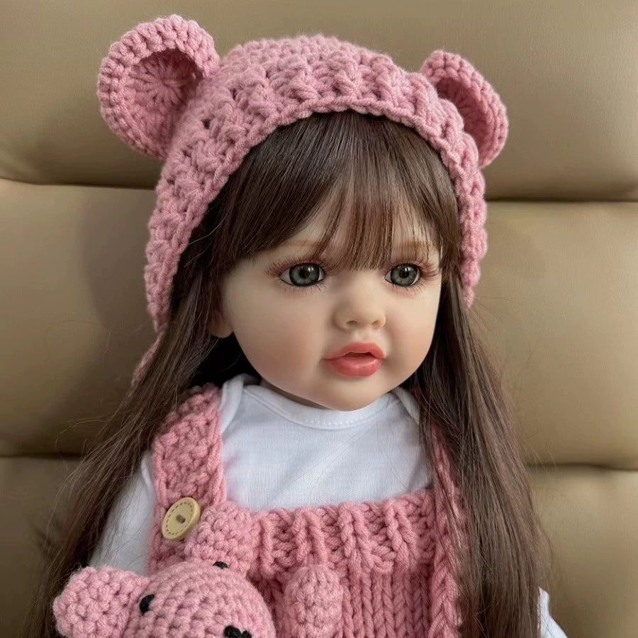 Child's doll wearing a pink knitted outfit with bear ears on a beige background